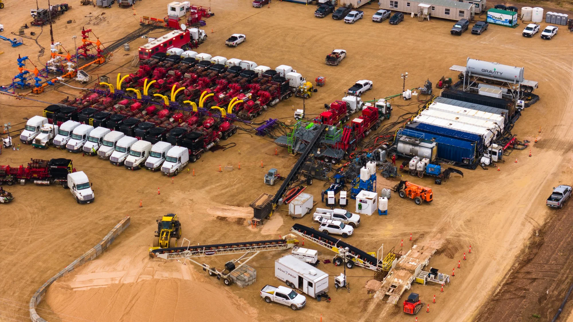 A construction site with various equipment and vehicles, including trucks, pipelines, and machinery, on a dirt lot.