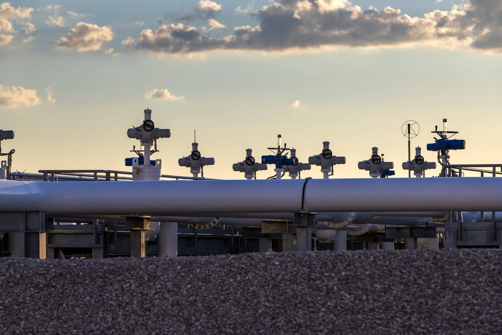 Industrial pipeline with valves and gauges under a cloudy sky.