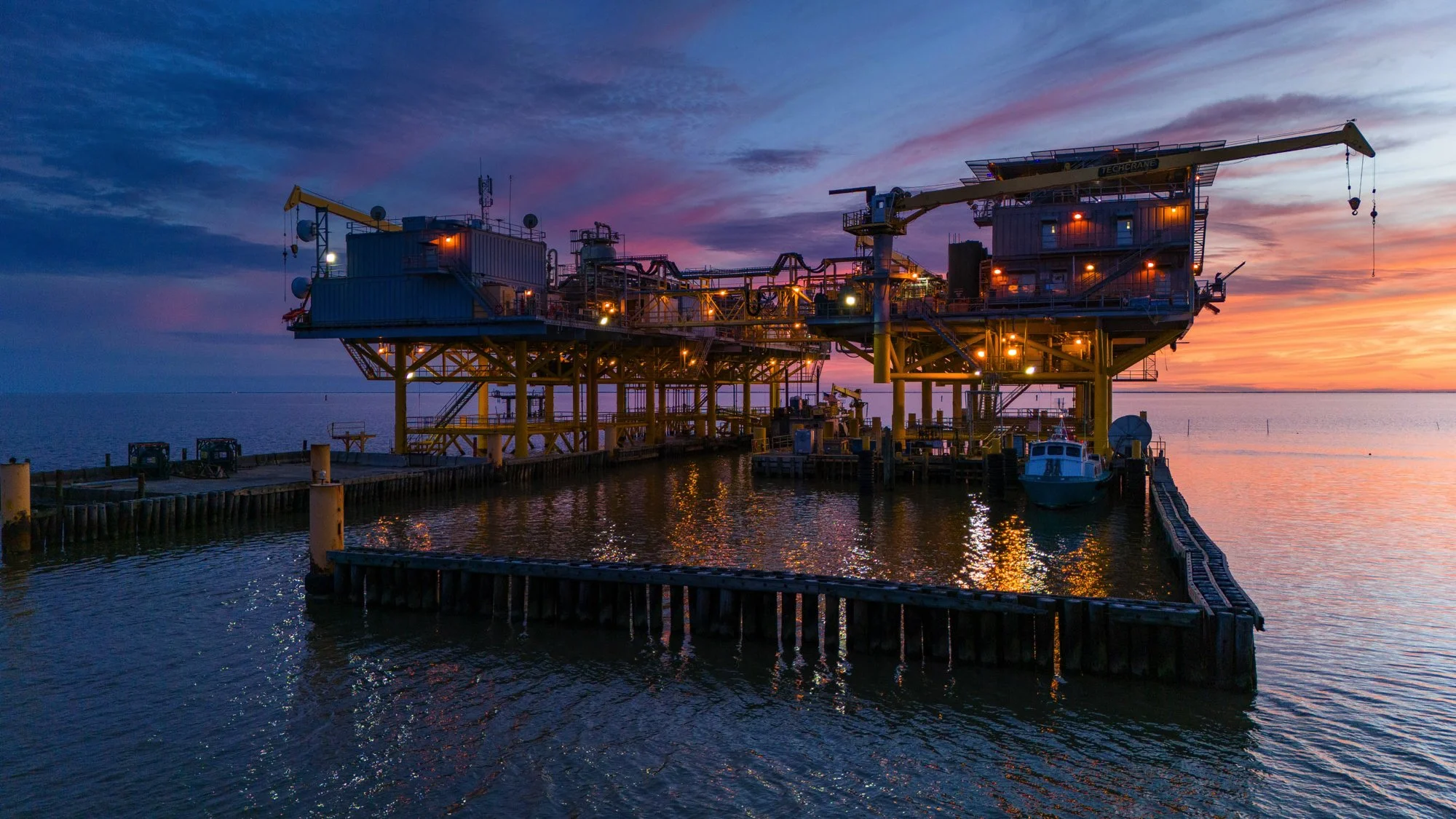 Oil rig structure at sunset in a body of water with a small boat docked nearby.