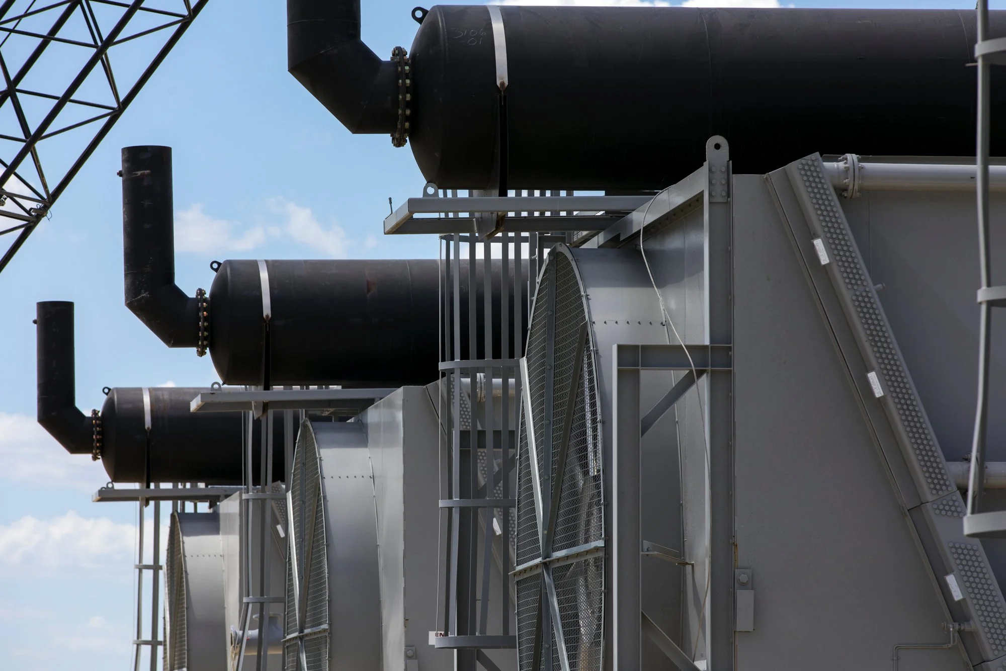 Close-up view of industrial HVAC units with black exhaust pipes and metallic grilles against a blue sky with clouds.
