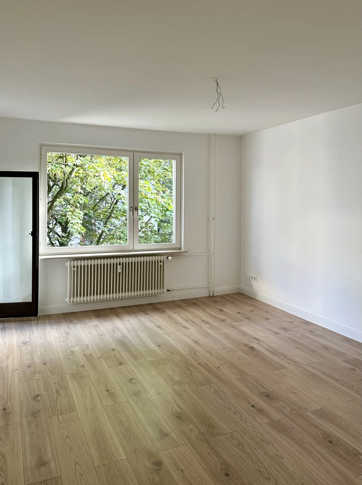 Leeres Zimmer mit großen Fenster, Holzfußboden und weiß gestrichenen Wänden.