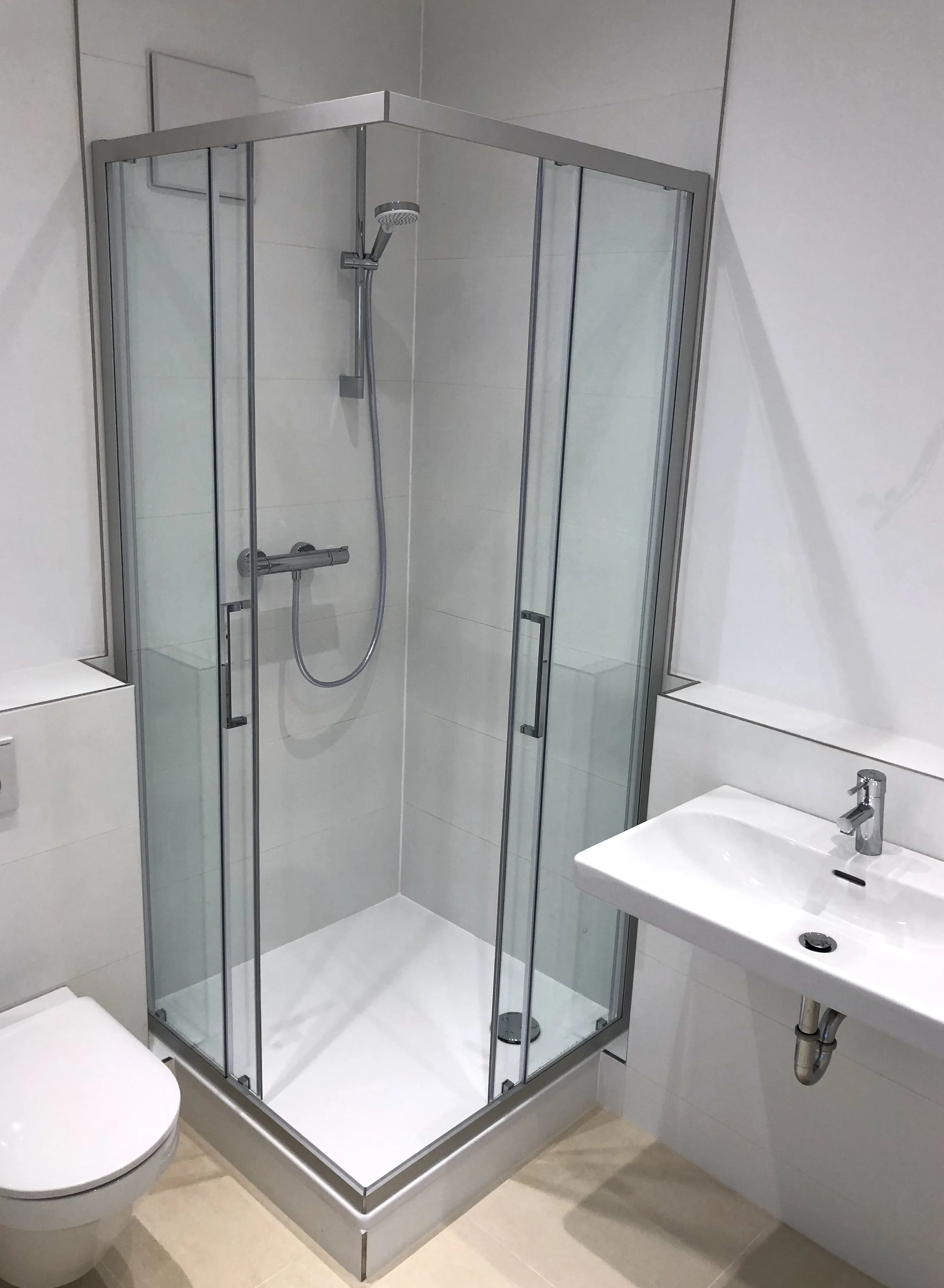 Ein moderner Badezimmerbereich mit einer Glas-Duschkabine, einem weißen Waschbecken und einem Toilettenbecken.