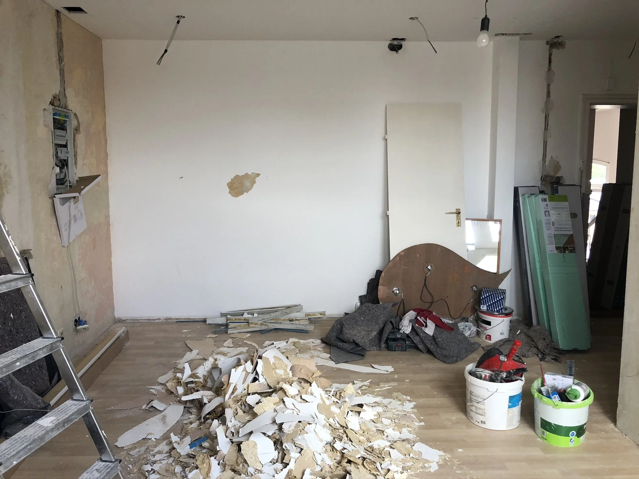 Raum im Umbau mit verstreutem Bauschutt, Werkzeug, Baumaterialien und unvollständiger Einrichtung.