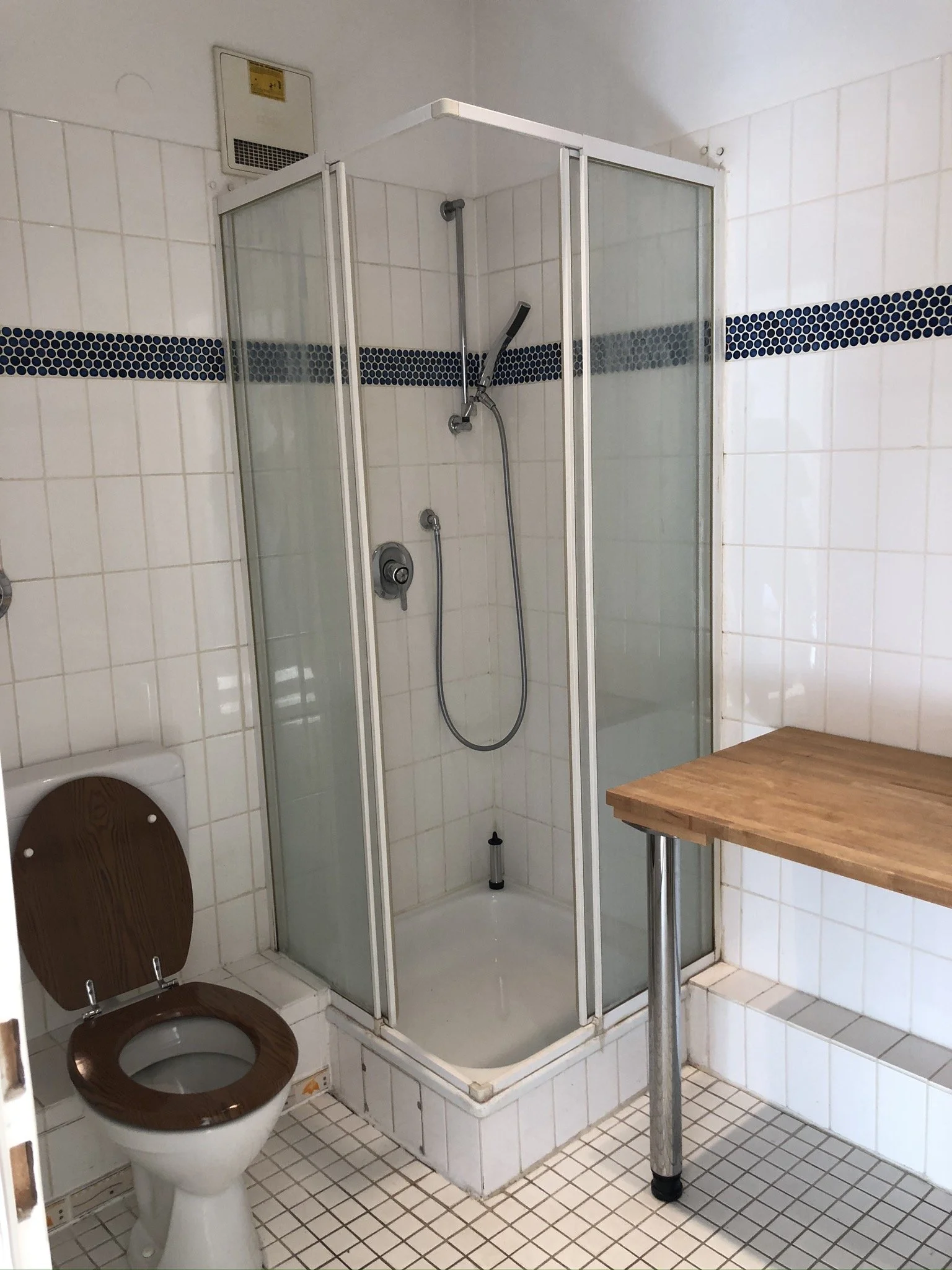 Ein Badezimmer mit Toilette, Duschkabine und einem Holztisch.