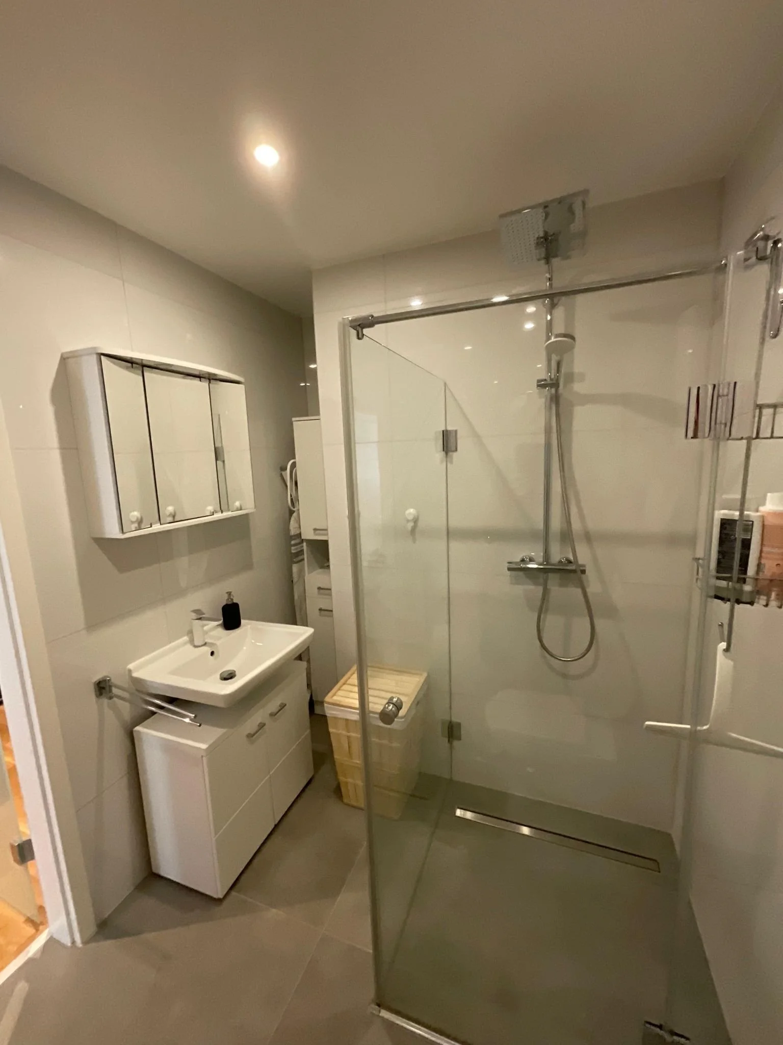 Ein modernes Badezimmer mit Dusche, Waschbecken, Spiegel und Waschmaschine.