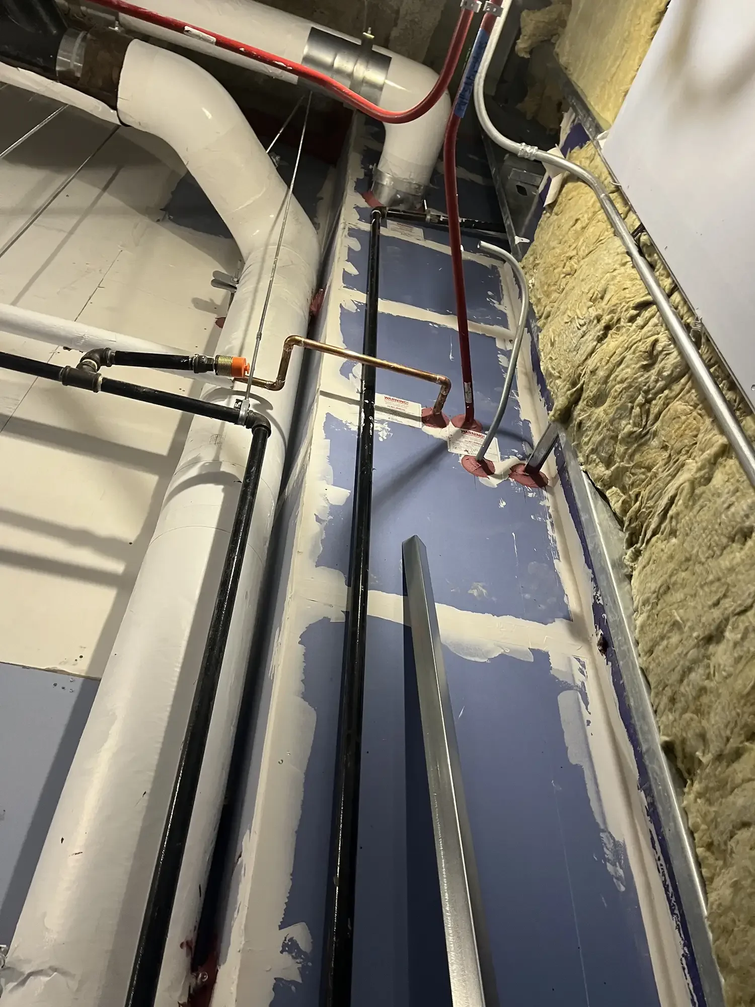 View of a construction or renovation site showing HVAC ductwork, pipes, and insulation on a partially finished wall and ceiling.