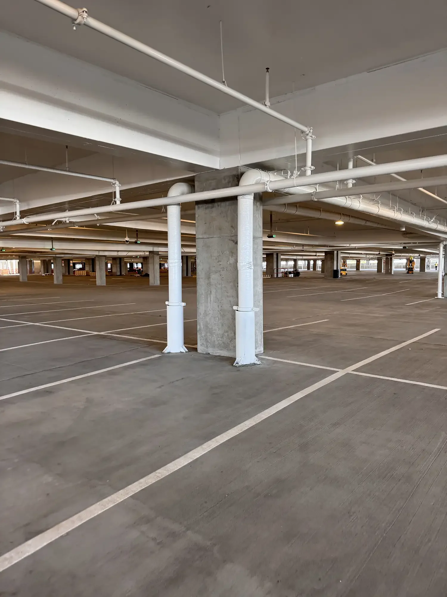 Empty multi-story parking garage with white pipes and concrete pillars.