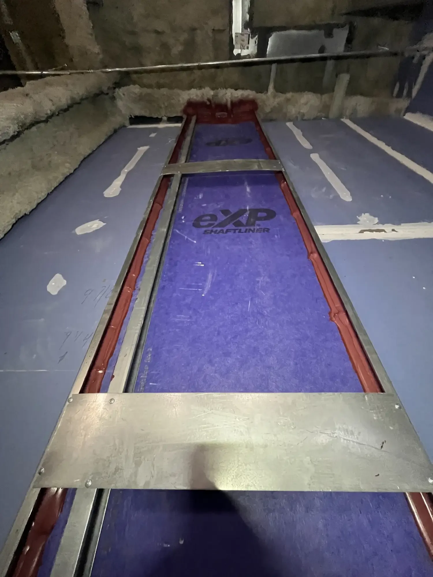 Construction site with metal framing and purple insulation labeled 'EXX' and 'SHATTLINER'.