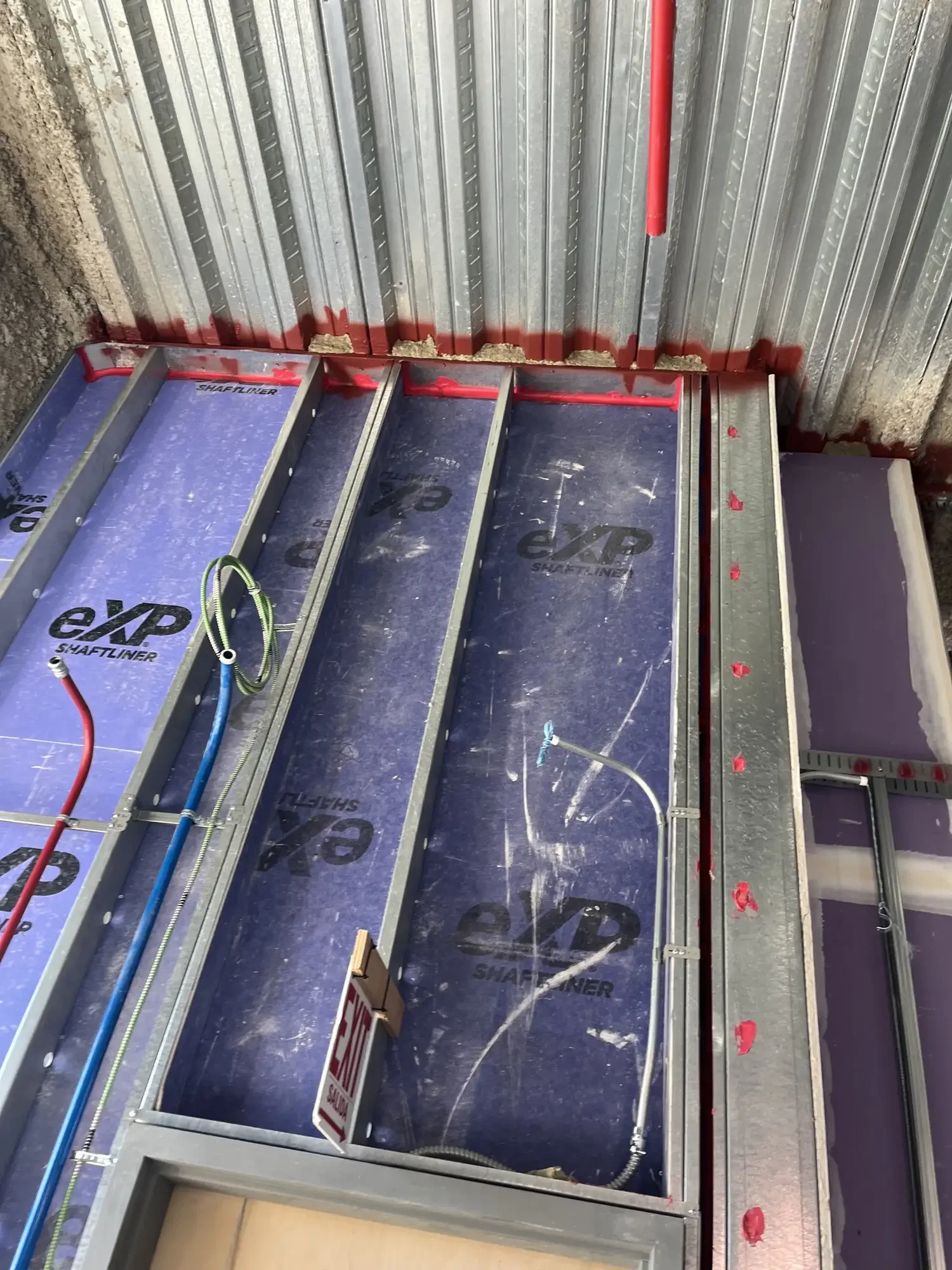 Interior of a building under construction with metal framing and wiring, with debris on the floor.