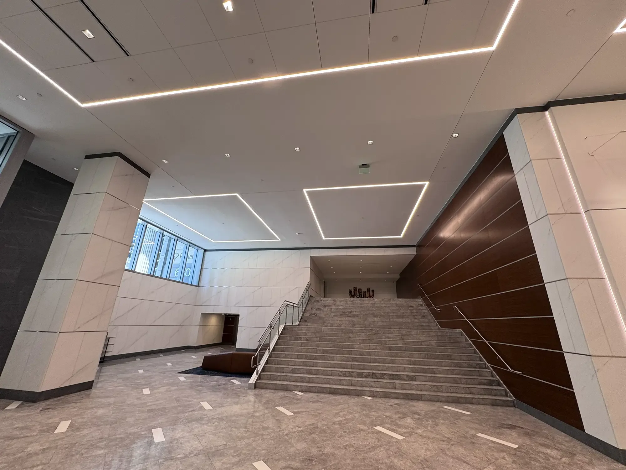 Interior lobby area with stairs, modern ceiling lighting, marble walls, and large windows.