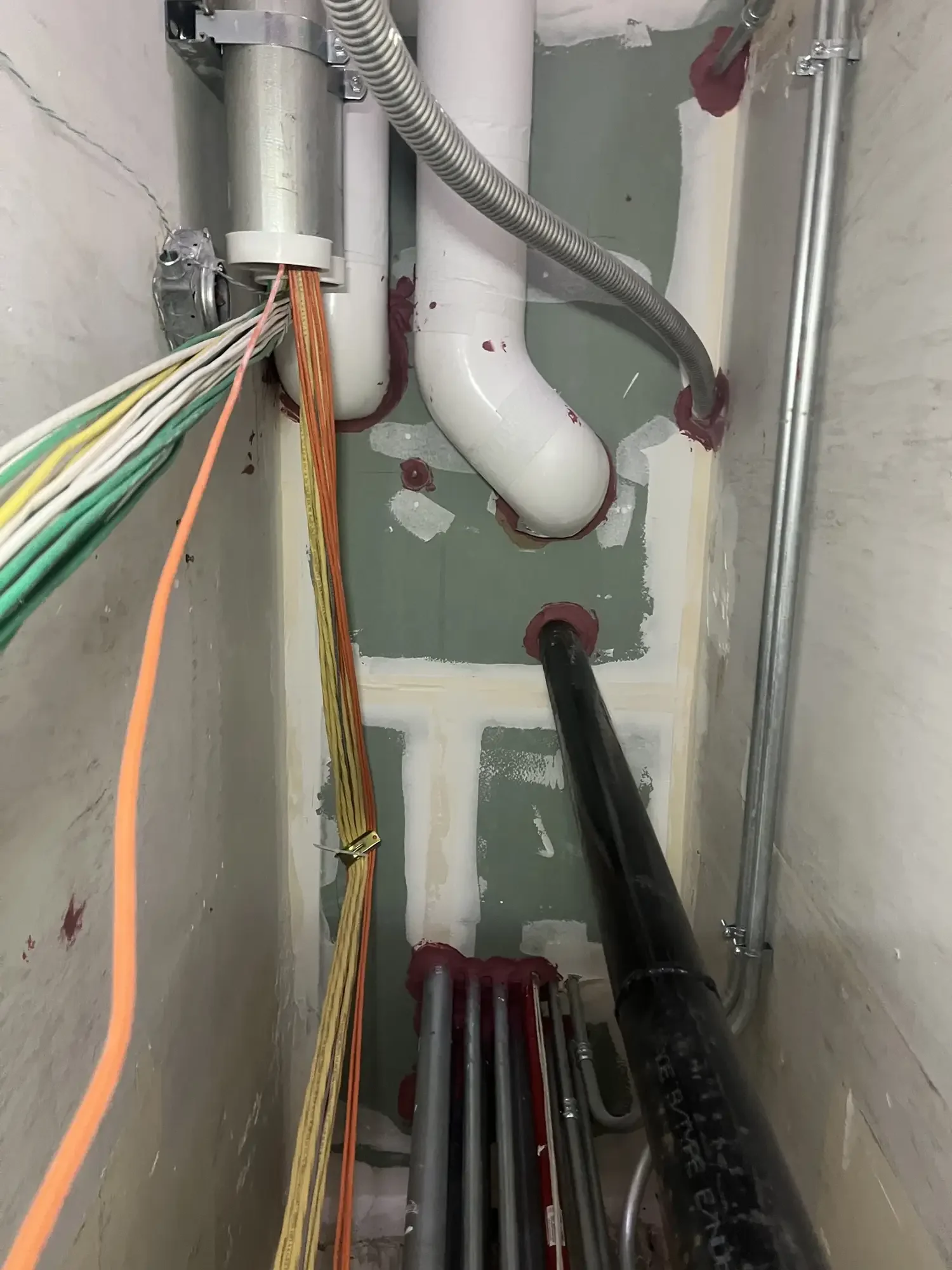 Installation of pipes and cables inside a utility access panel or crawl space, with visible plumbing, electrical wiring, and conduit mounting brackets.