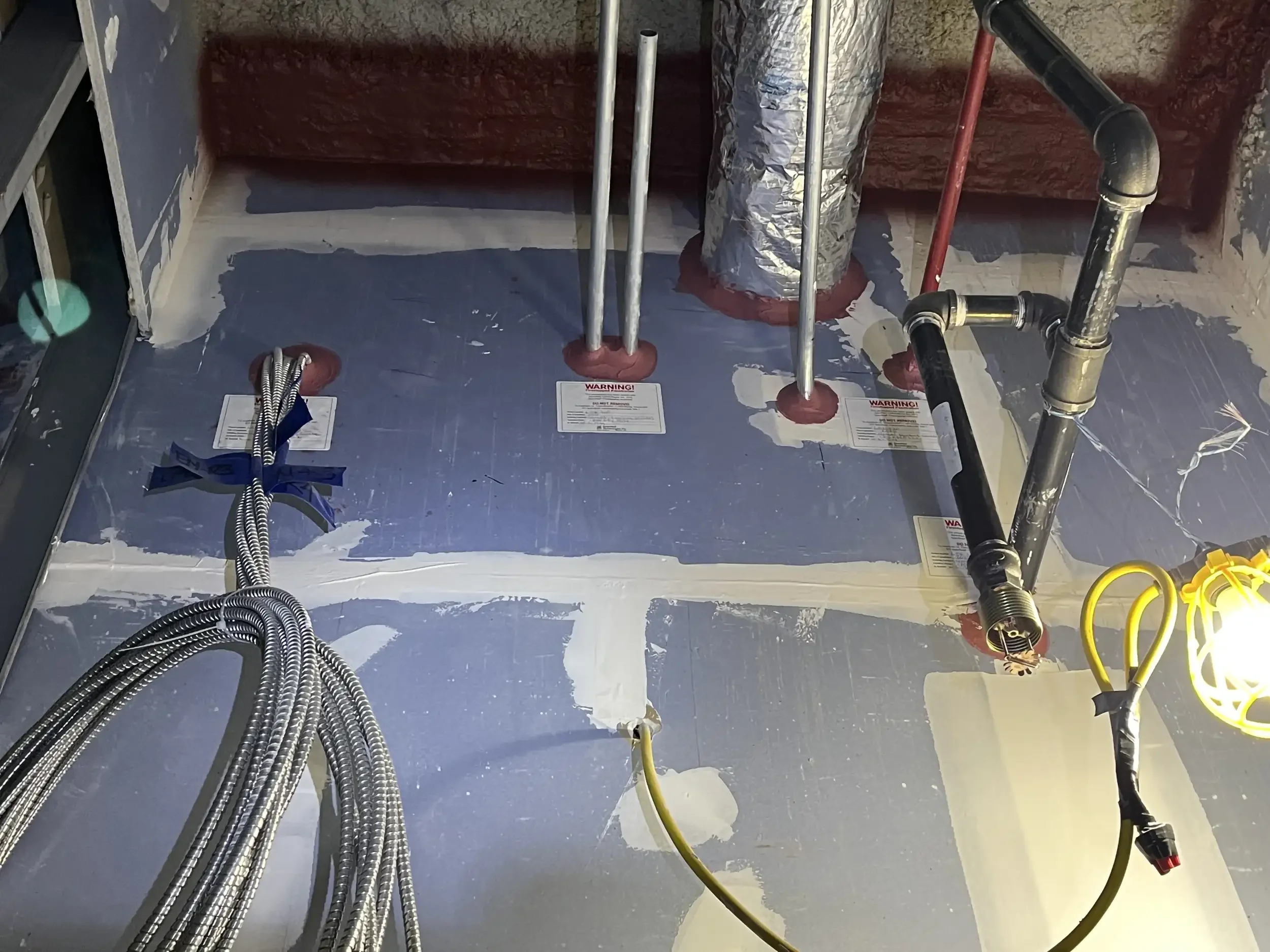 View of a construction or plumbing area with exposed pipes, wires, and insulation materials, suggesting ongoing installation work.