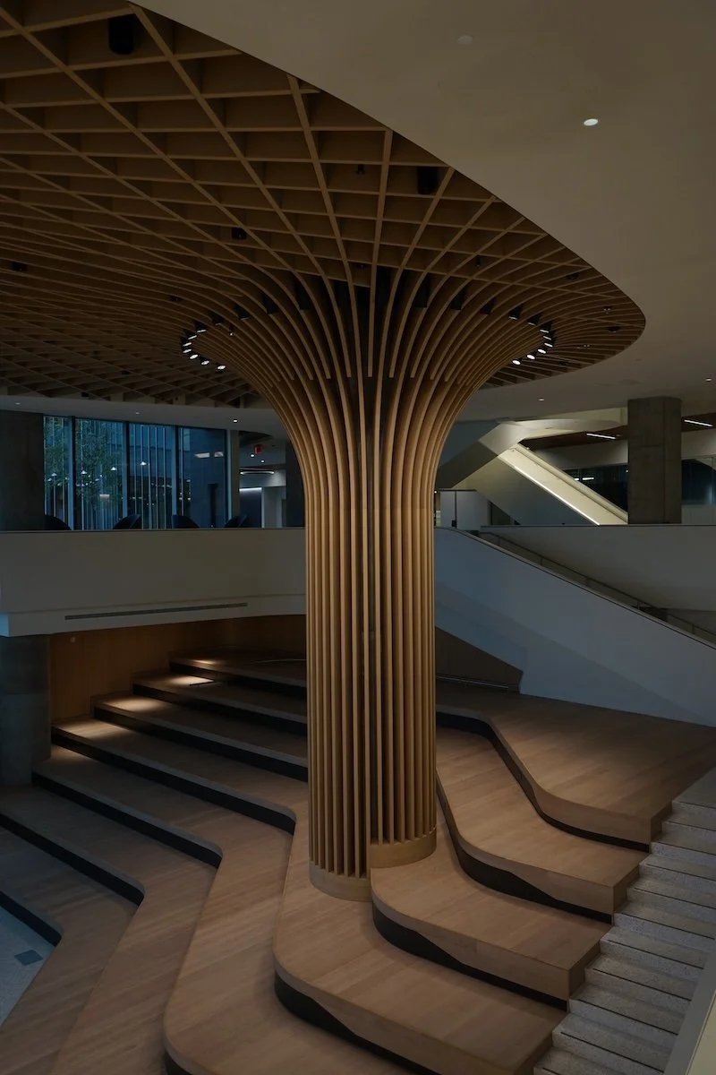 Interior of a modern building featuring a large sculptural wooden column with an intricate geometric ceiling design.
