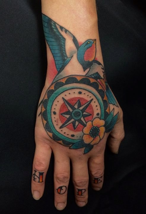 Tattoo of a bird, compass, and flower on a hand.