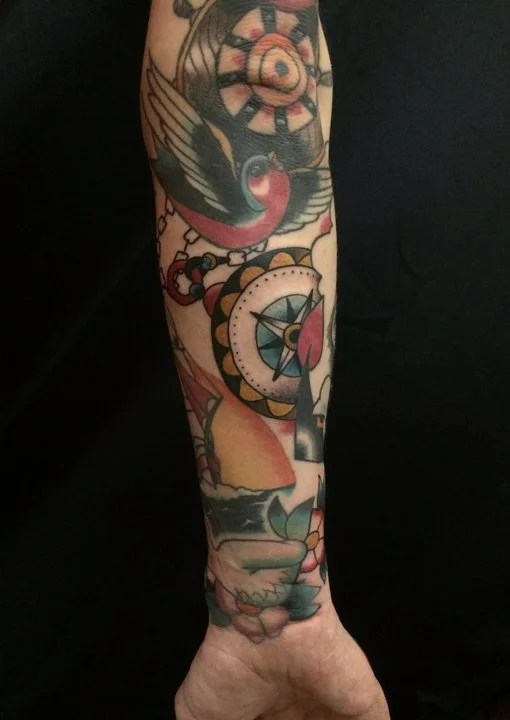 Tattoo sleeve on person's forearm featuring a bird, compass, and floral elements.