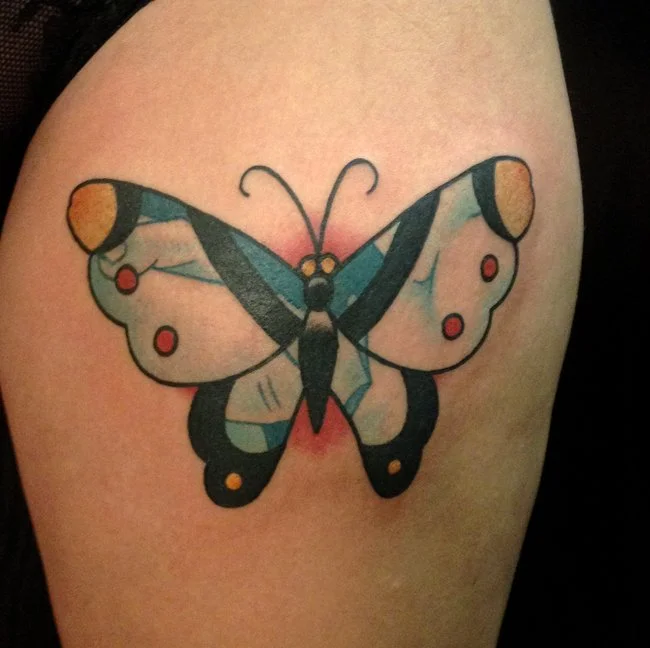 Colorful butterfly tattoo on skin with vibrant orange, black, blue, and pink hues.