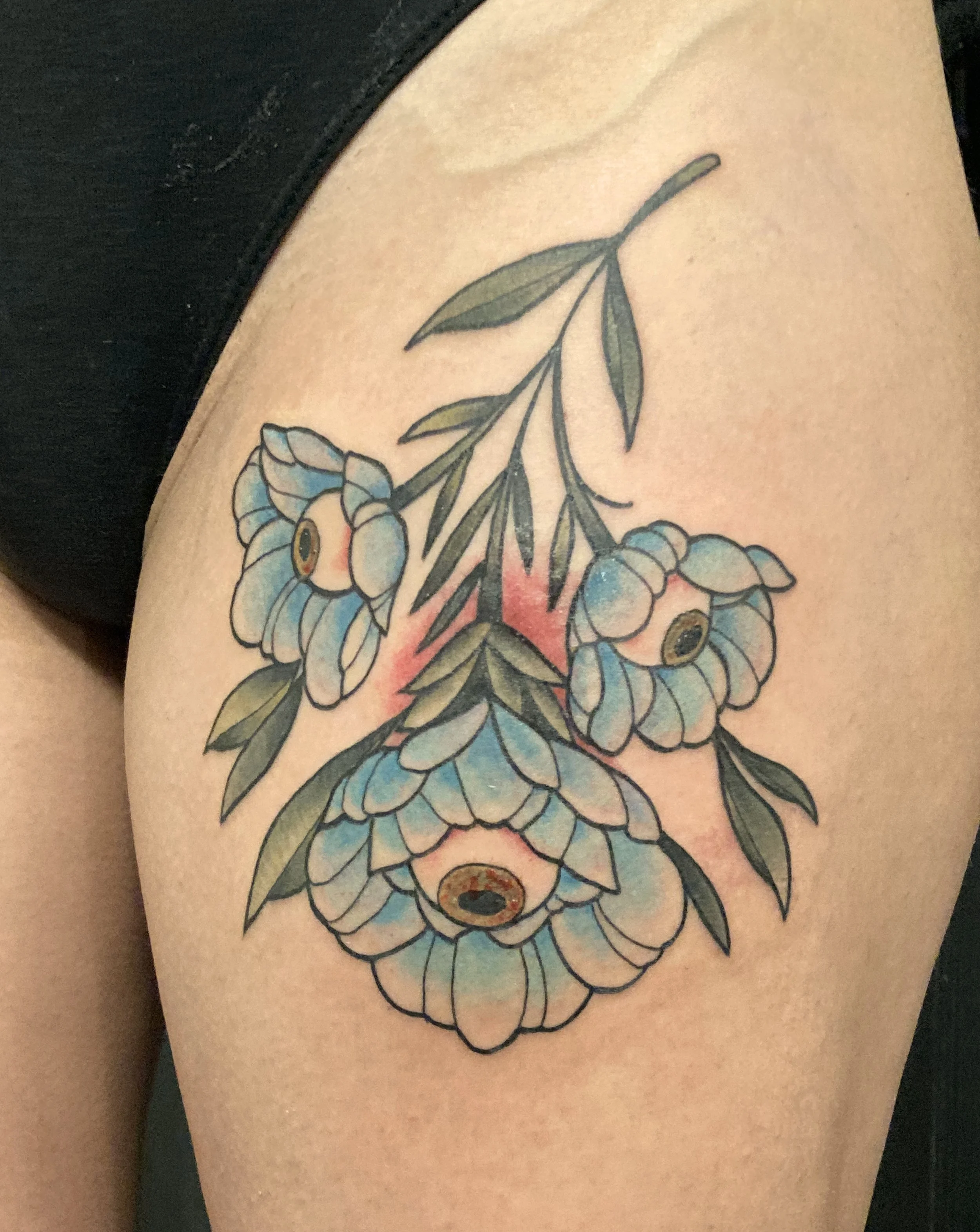Tattoo of a blue and green floral design with multiple flowers and leaves on a hip.