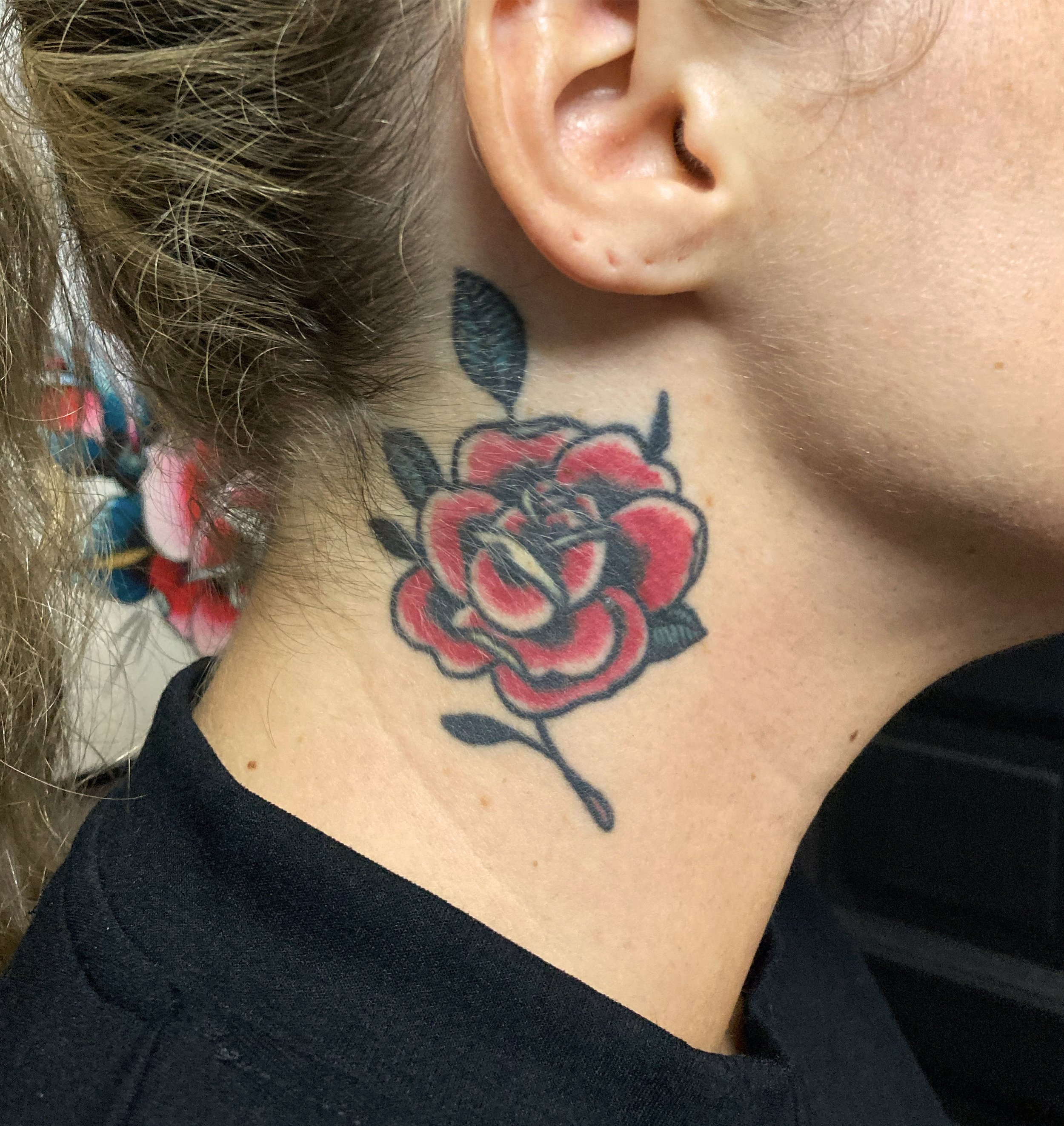 Tattoo of a red and black rose on the neck, near the ear.