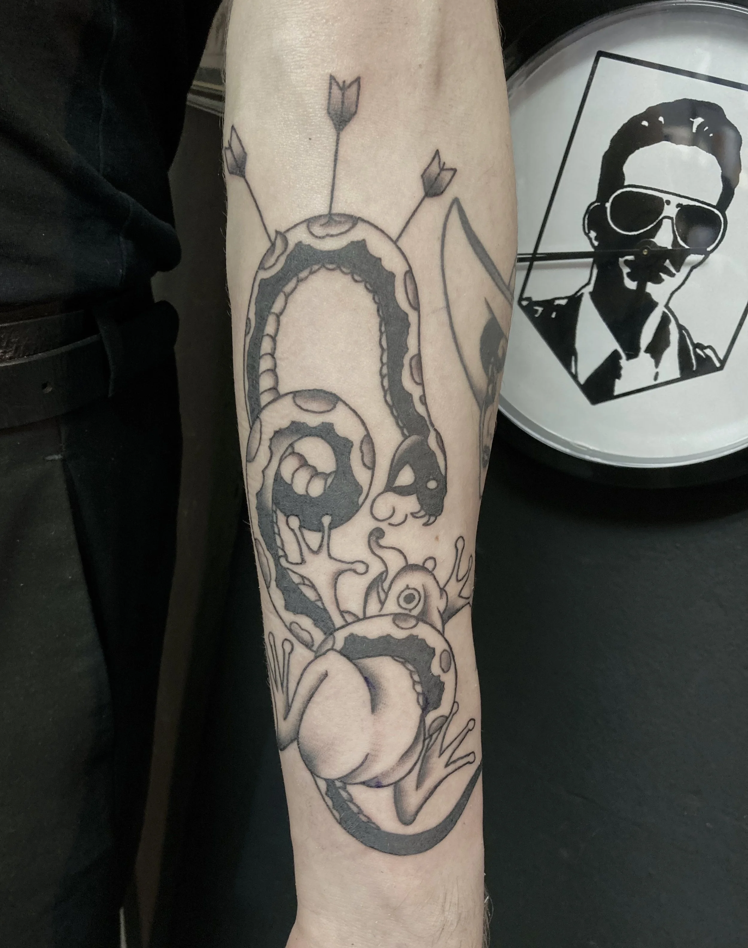 Tattoo of a snake coiled around a frog on a person's forearm.