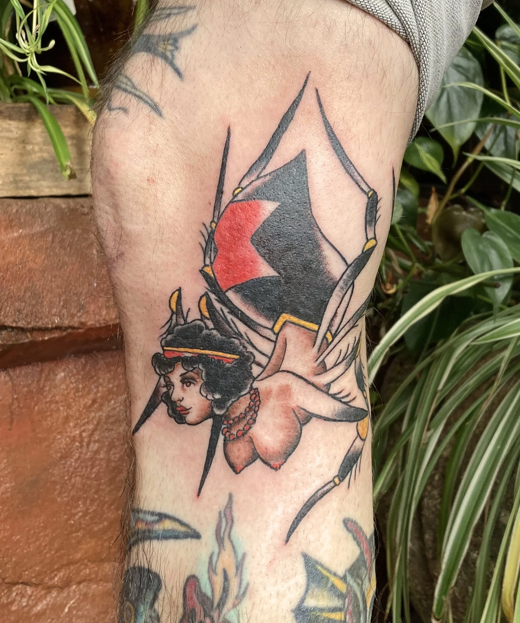 Tattoo of a spider-woman with dark curly hair, amid a spider web with red and black design.