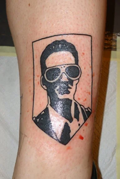 Tattoo of a man wearing sunglasses inside a rectangular frame.