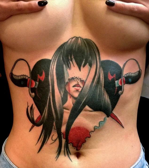 Tattoos of a woman with long black hair and hooded eyes, with a heart-shaped background, on the stomach.