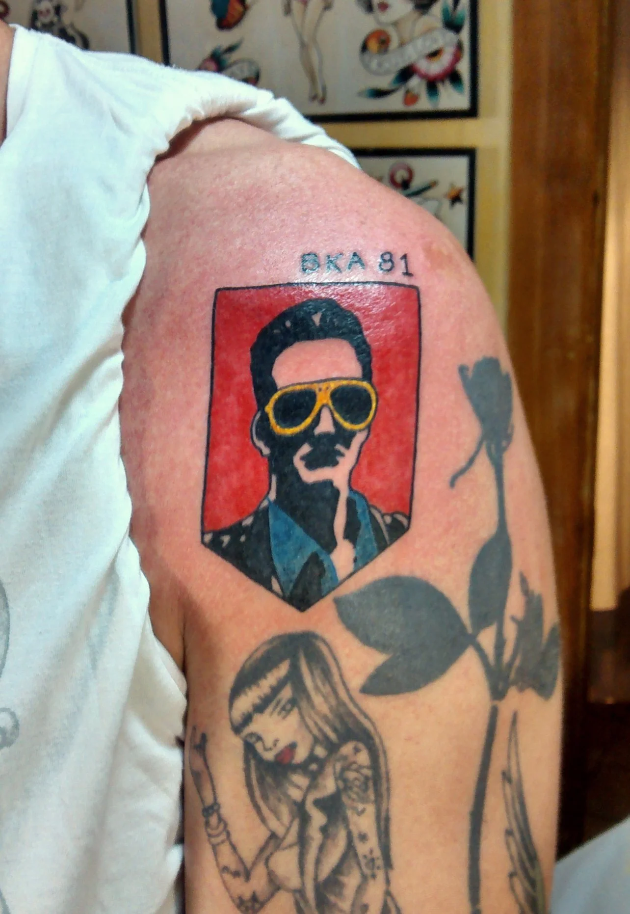 Tattoo of a stylized portrait of a man wearing yellow sunglasses, with the text 'BKA 81' above, on a person's upper arm.