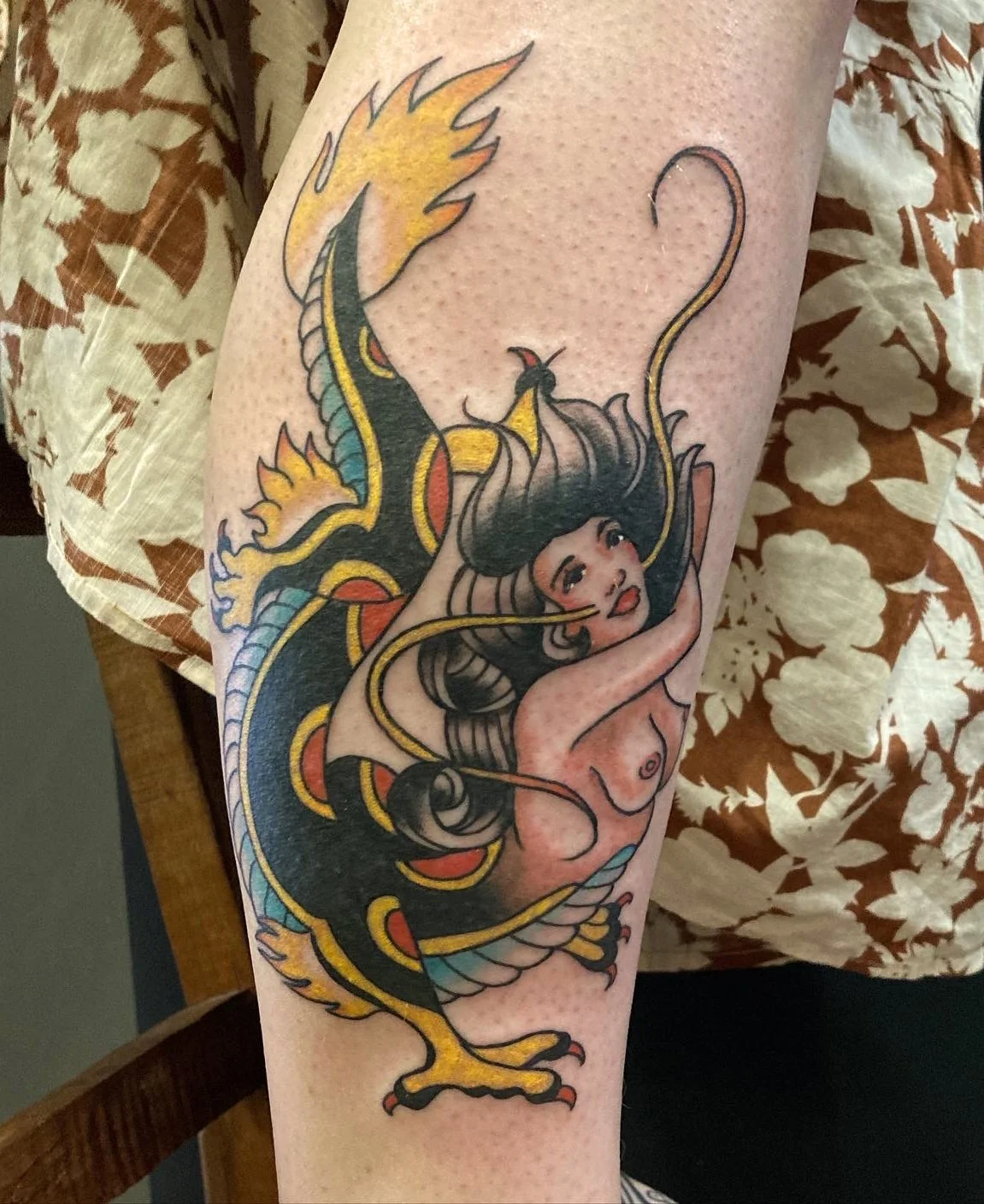 Tattoo of a woman with long black hair intertwined with a dragon on a person's arm.