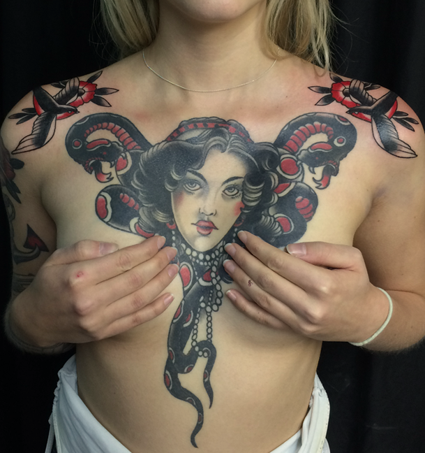A person with a tattoo of Medusa on their chest, covering the area from the shoulders to the upper stomach, with snakes and a woman's face at the center.