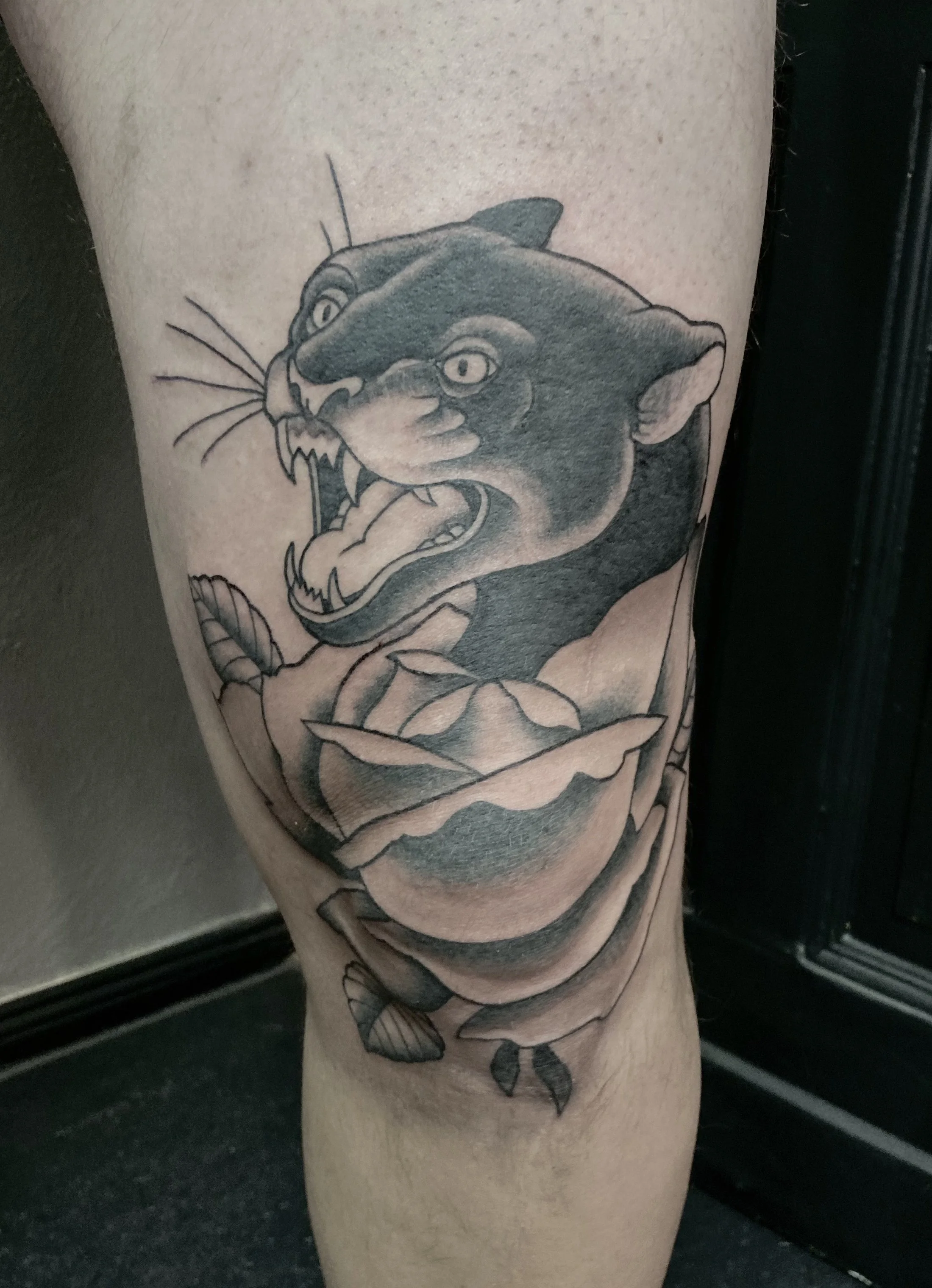 Tattoo of a snarling panther on a person's leg, with detailed shading and a flower at the base of the panther's neck.