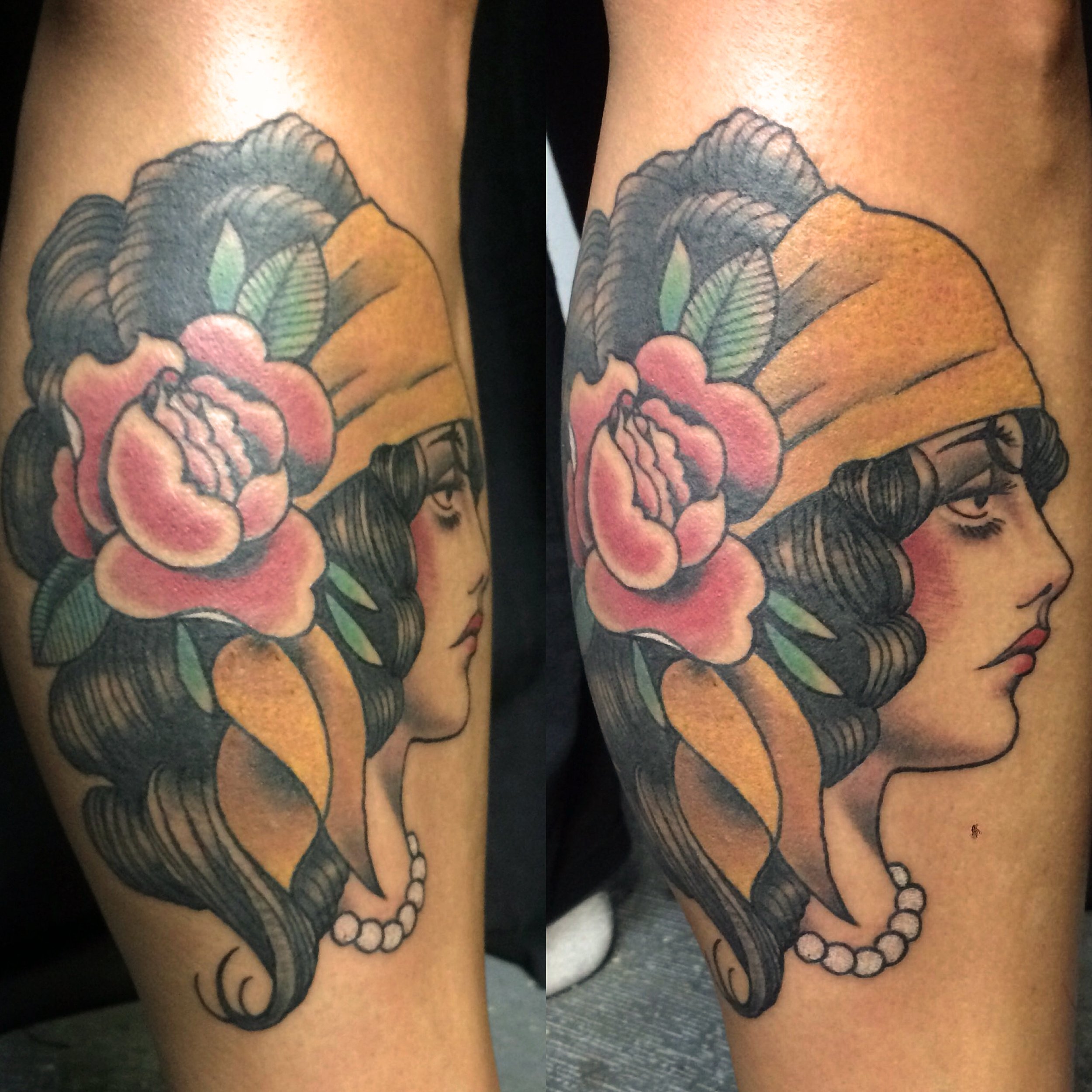 Tattoo of a woman with dark hair, pink flowers, green leaves, a yellow headband, and a pearl necklace, drawn in a traditional style.
