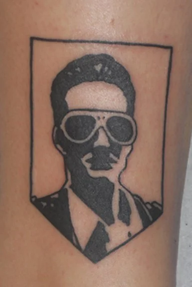 Tattoo of a man with sunglasses inside a rectangular frame.