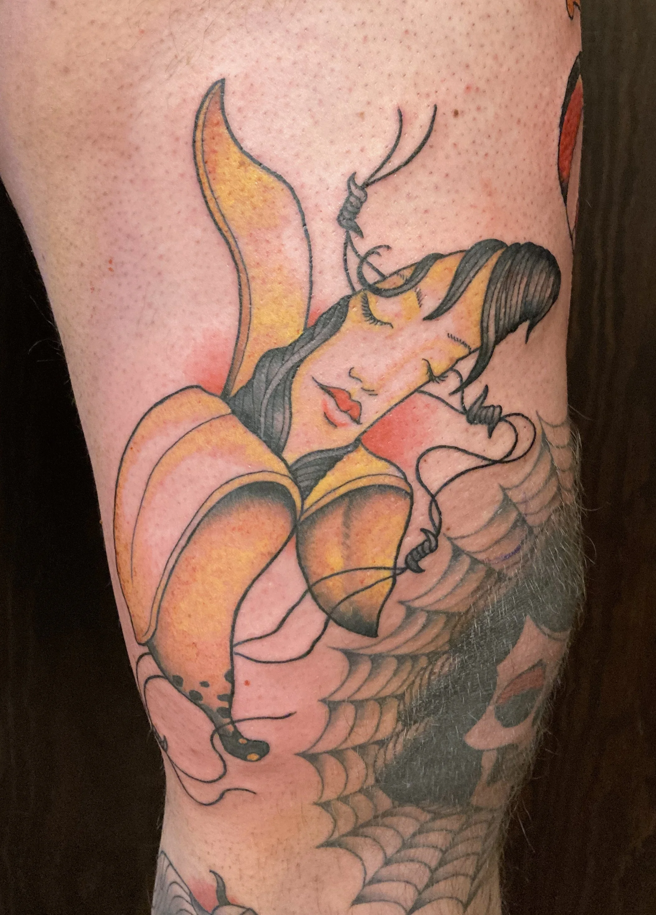 Tattoo of a banana woman, with dark hair covering her face, surrounded by barb wire.