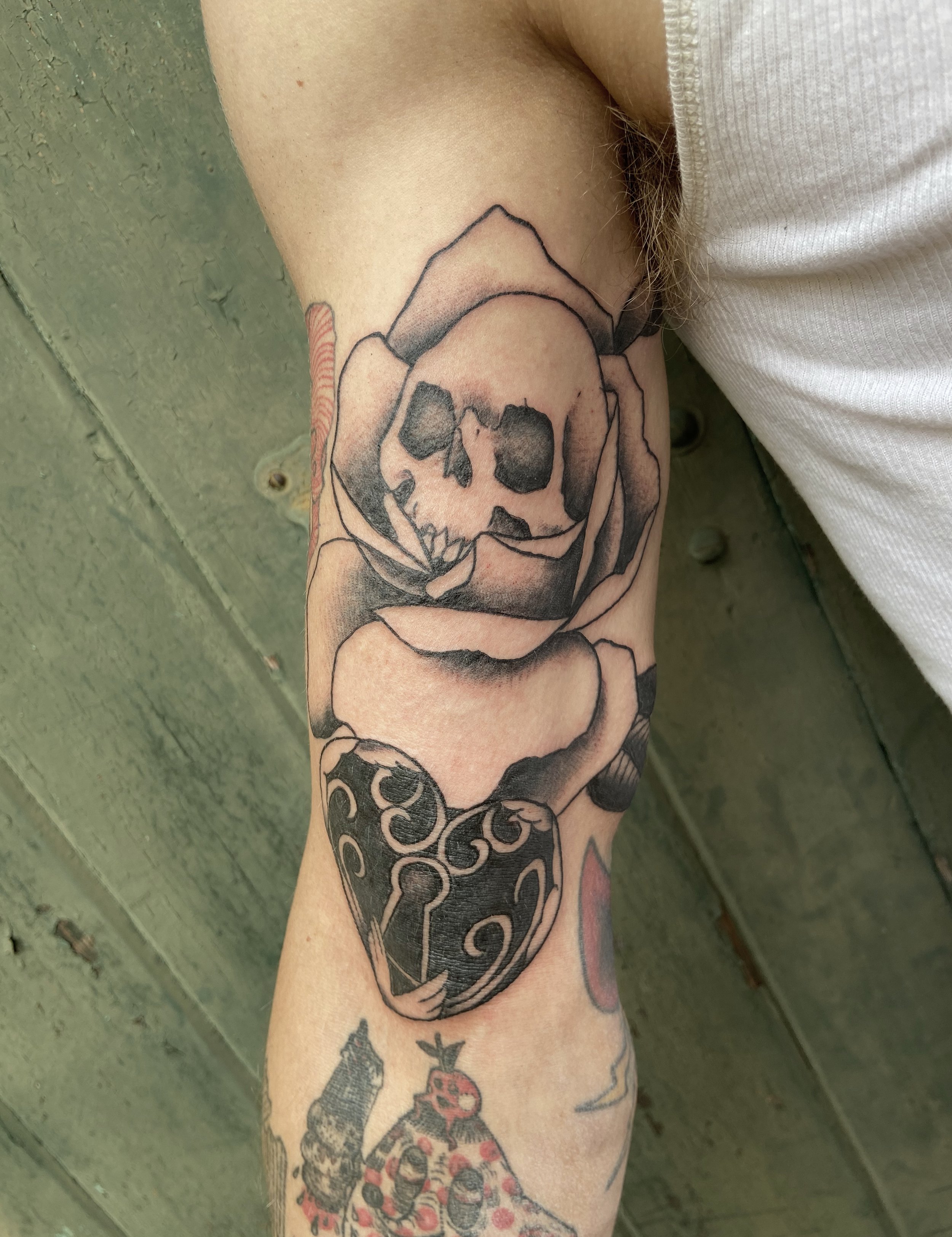 Tattoo of a skull inside a rose, with a keyhole at the bottom, on a person's arm.