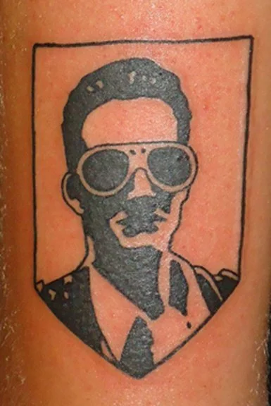 Tattoo of a person wearing sunglasses, outlined within a rectangle.