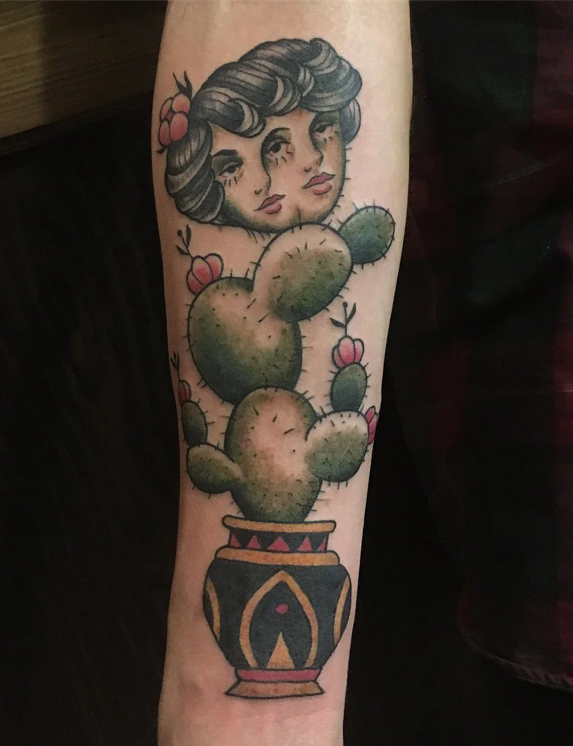 Tattoo of a woman with historic facial features and hair, surrounded by pink flowers, emerging from a cactus in a patterned pot.