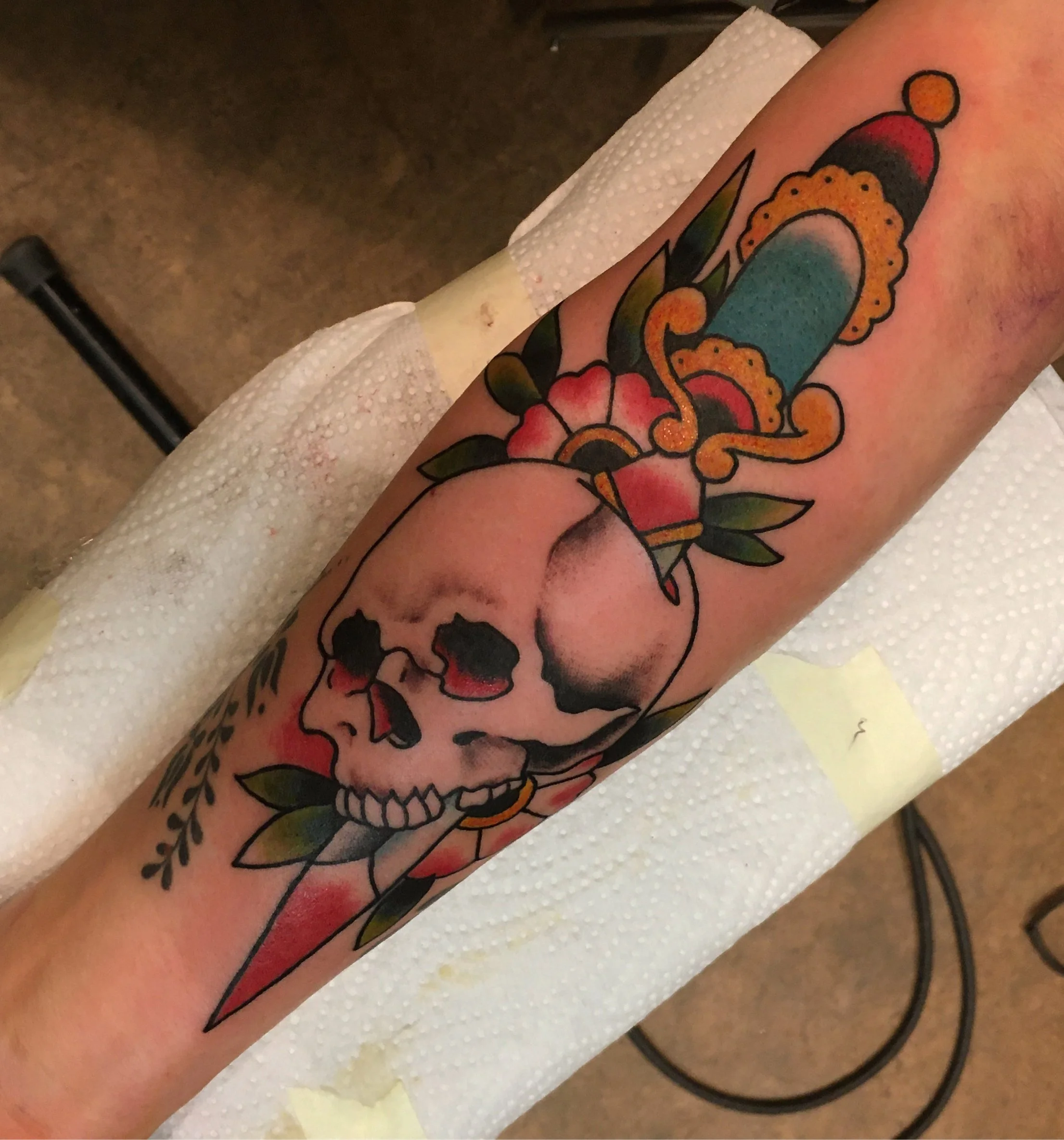 A colorful tattoo of a skull with floral and geometric elements on a person's forearm.