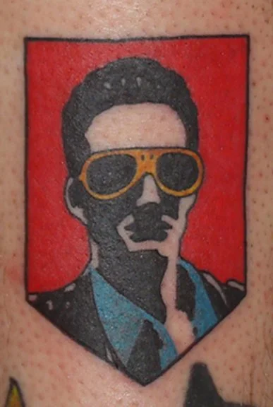 Tattoo of a person wearing yellow sunglasses, set against a red background.