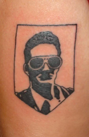 Tattoo of a man wearing glasses, enclosed within a rectangular frame.