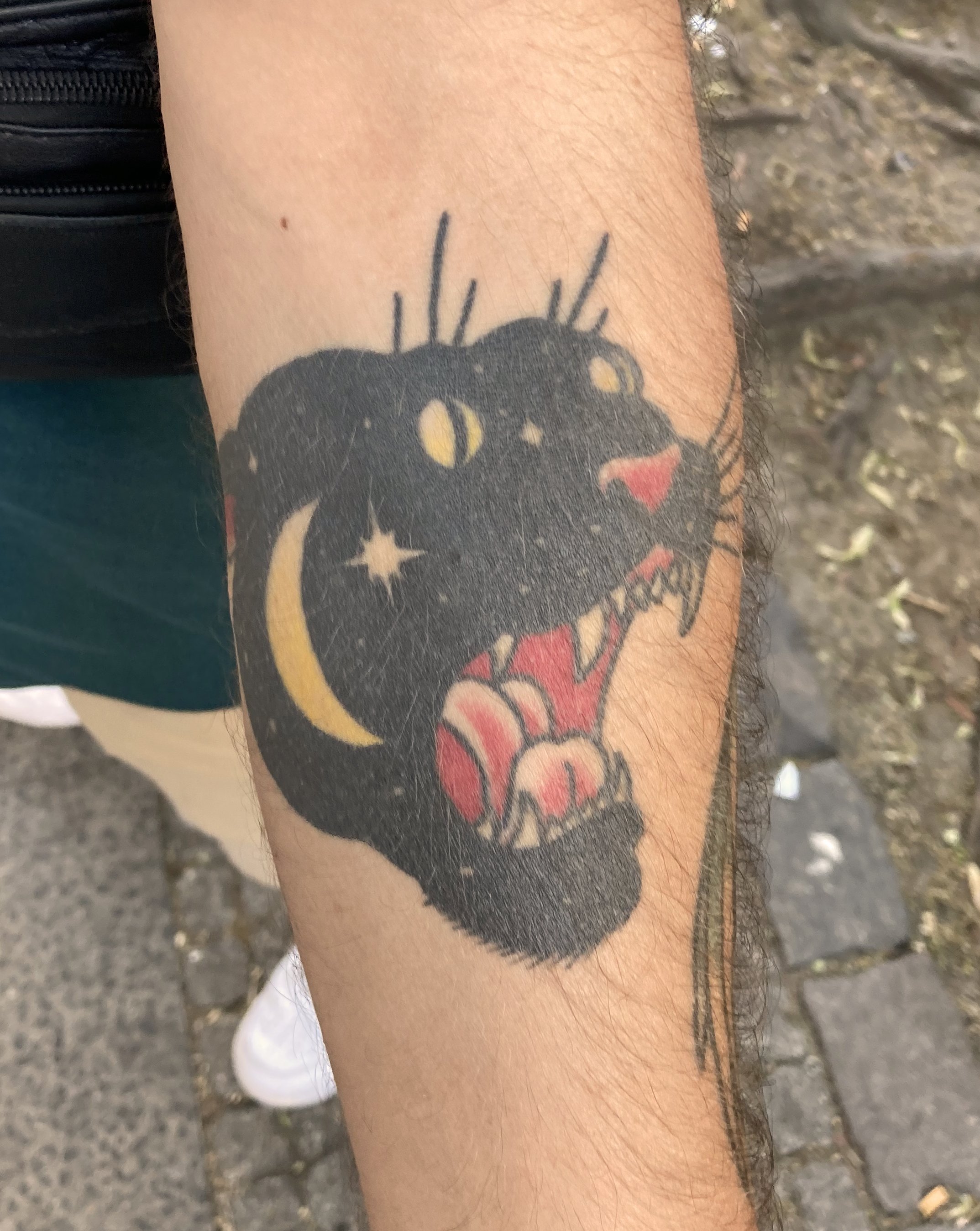 Tattoo of a black panther with yellow eyes, stars, crescent moon, and red tongue on person's arm.