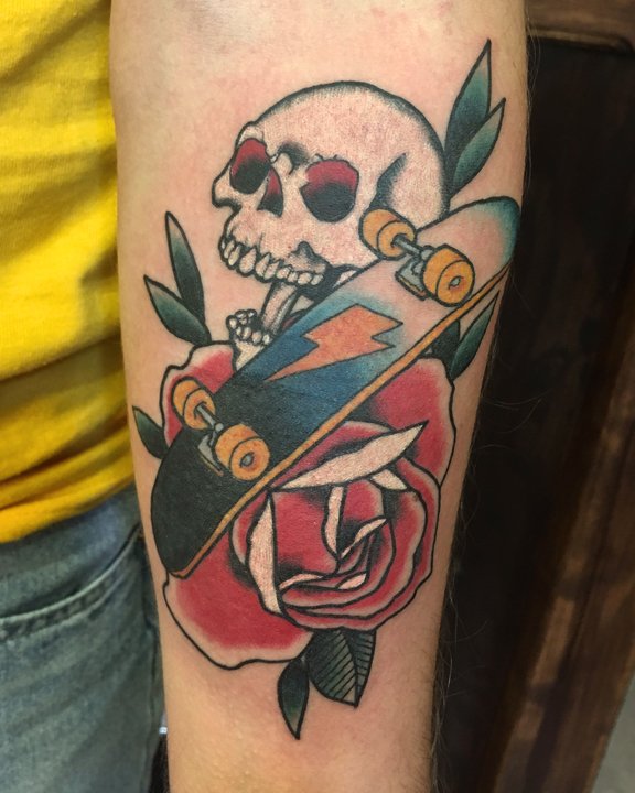 Tattoo of a skull, skateboard, and rose with leaves on a person's arm.
