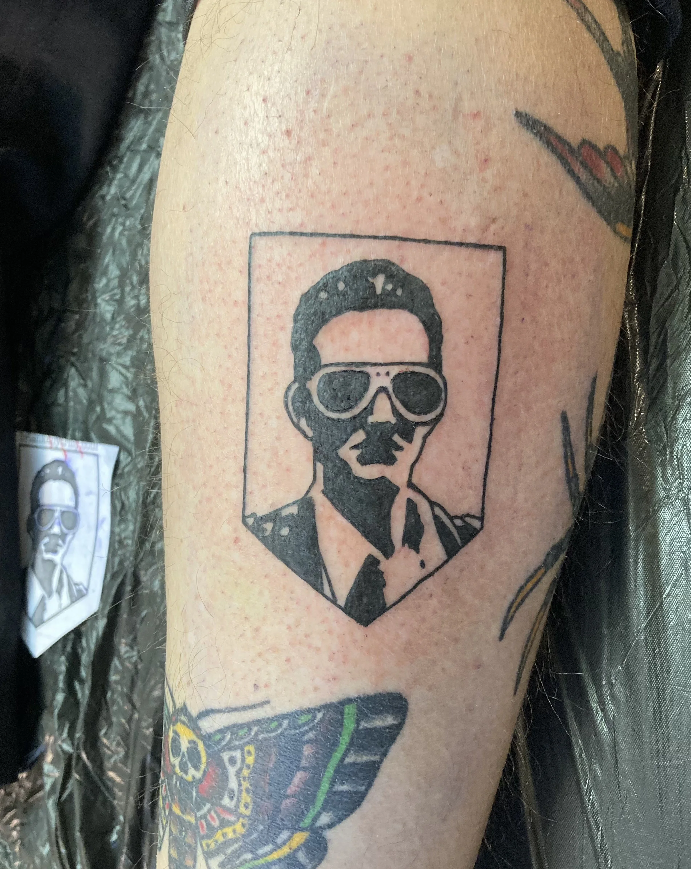 Tattoo of a man wearing sunglasses inside a rectangular frame on upper arm.
