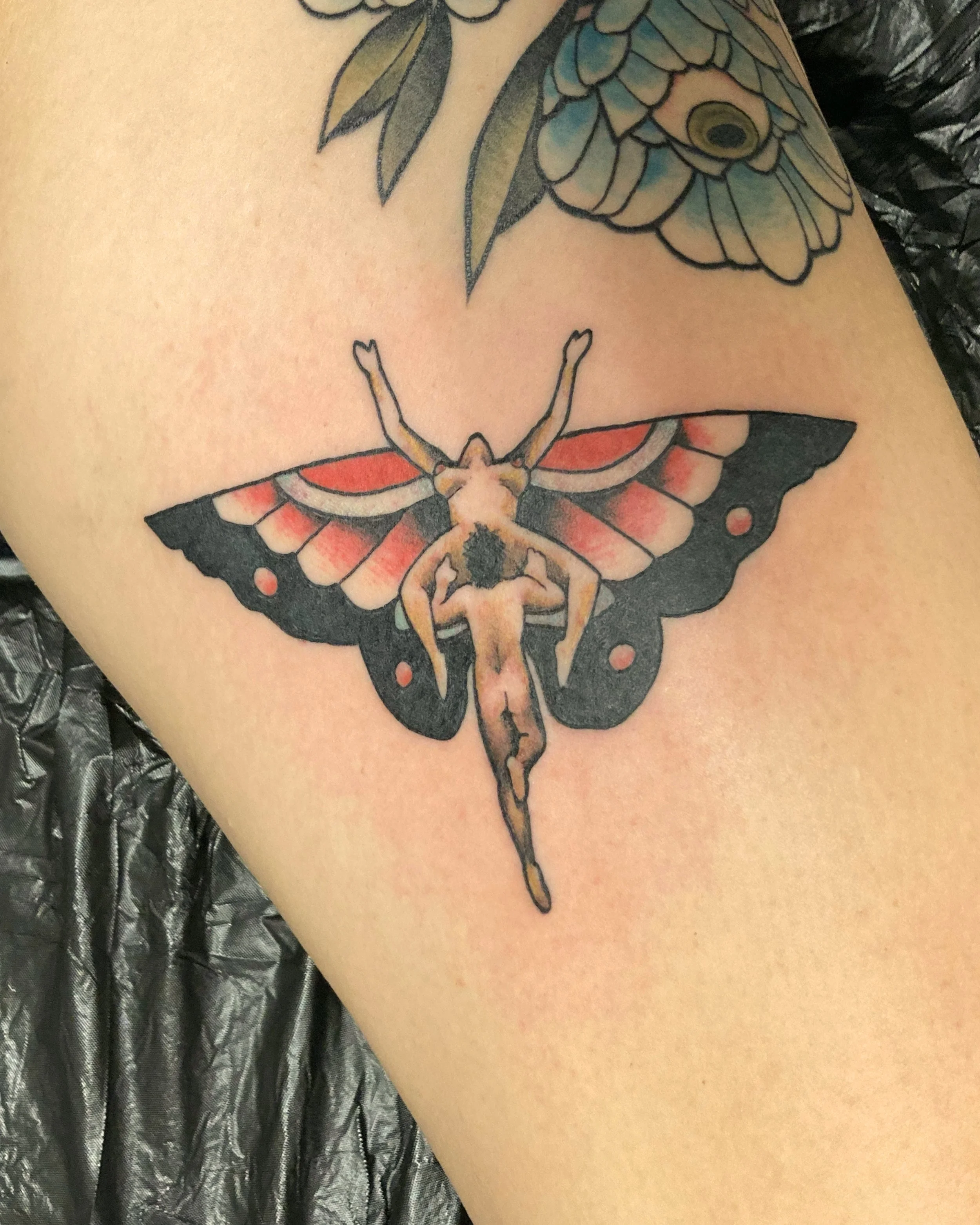 A tattoo of a butterfly with human legs and a human head, positioned on a person's leg.
