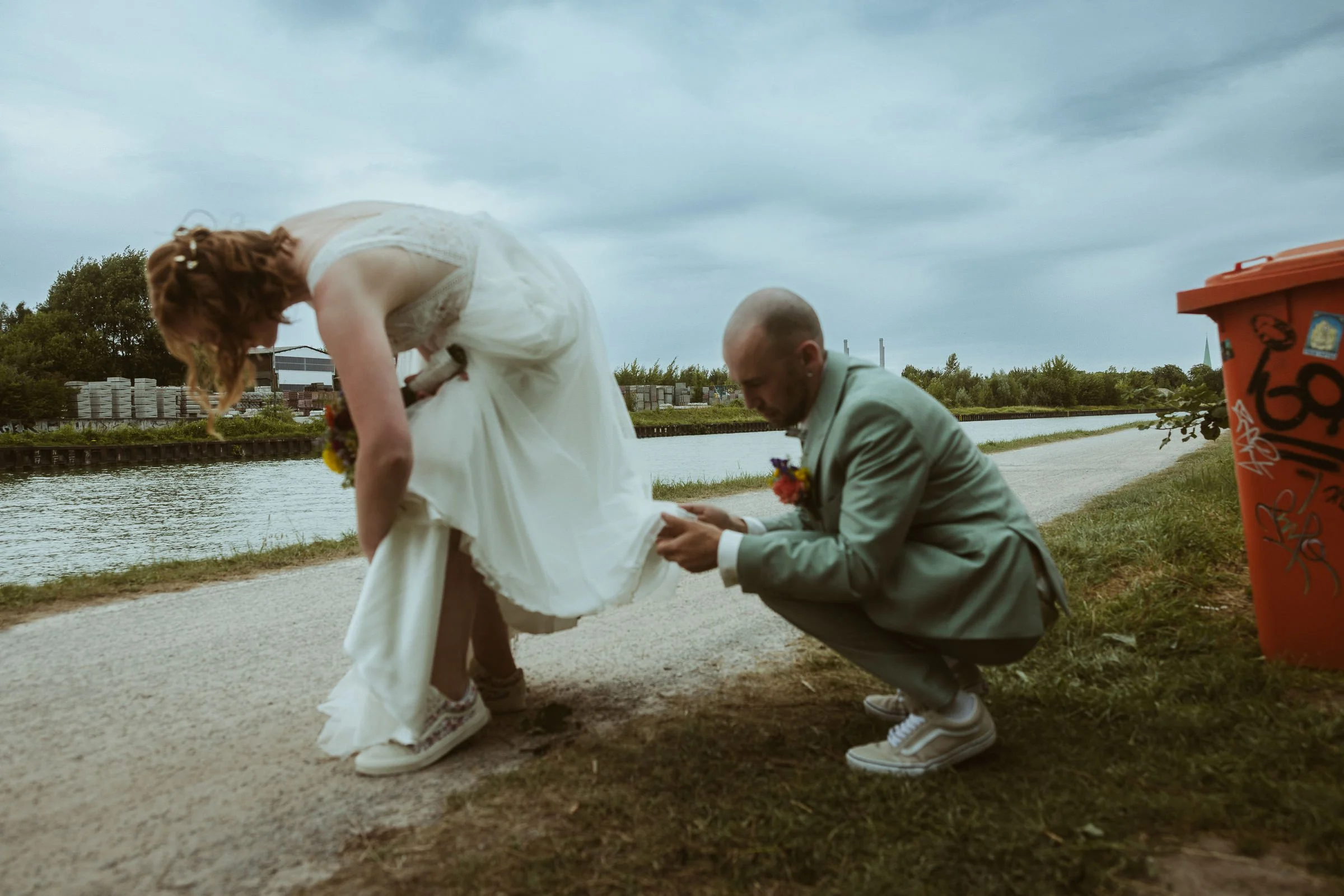 Bräutigam richtet das Brautkleid am Kanal bei einer unkonventionellen Hochzeit in Münster