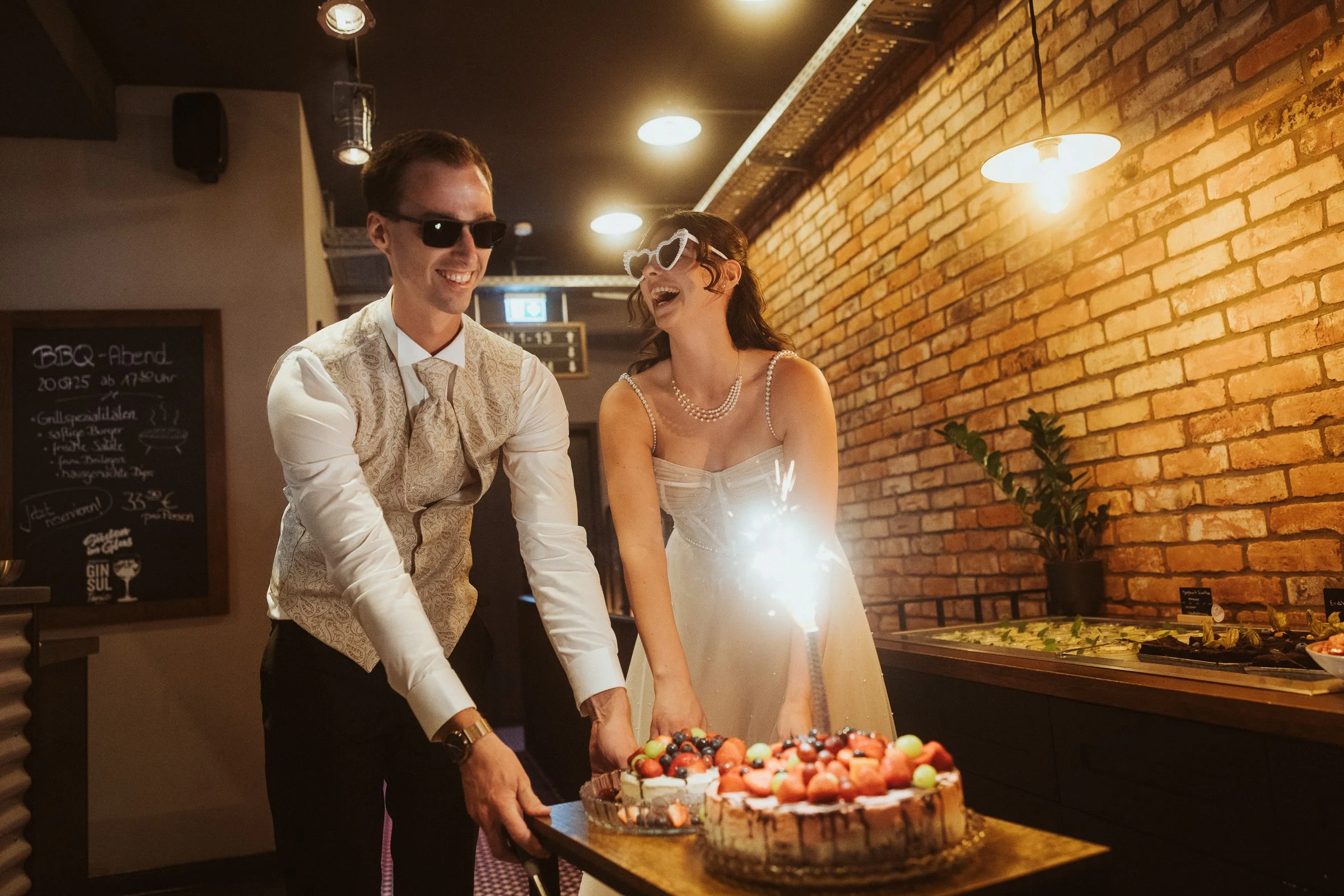 Lachendes Hochzeitspaar mit Sonnenbrillen und Hochzeitstorte im Fliegerdeich Wilhelmshaven