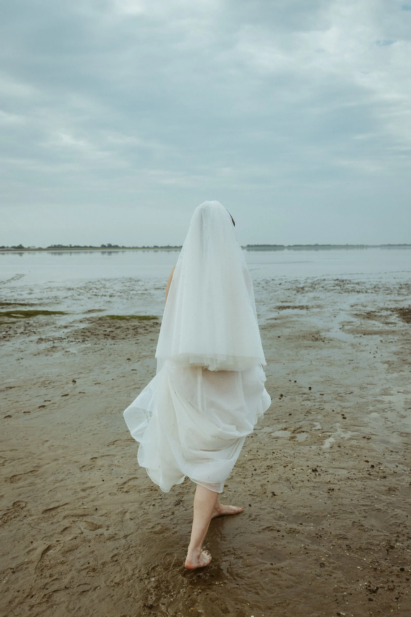 Braut läuft barfuß mit Schleier über den Strand bei einer Hochzeit in Hooksiel an der Nordsee