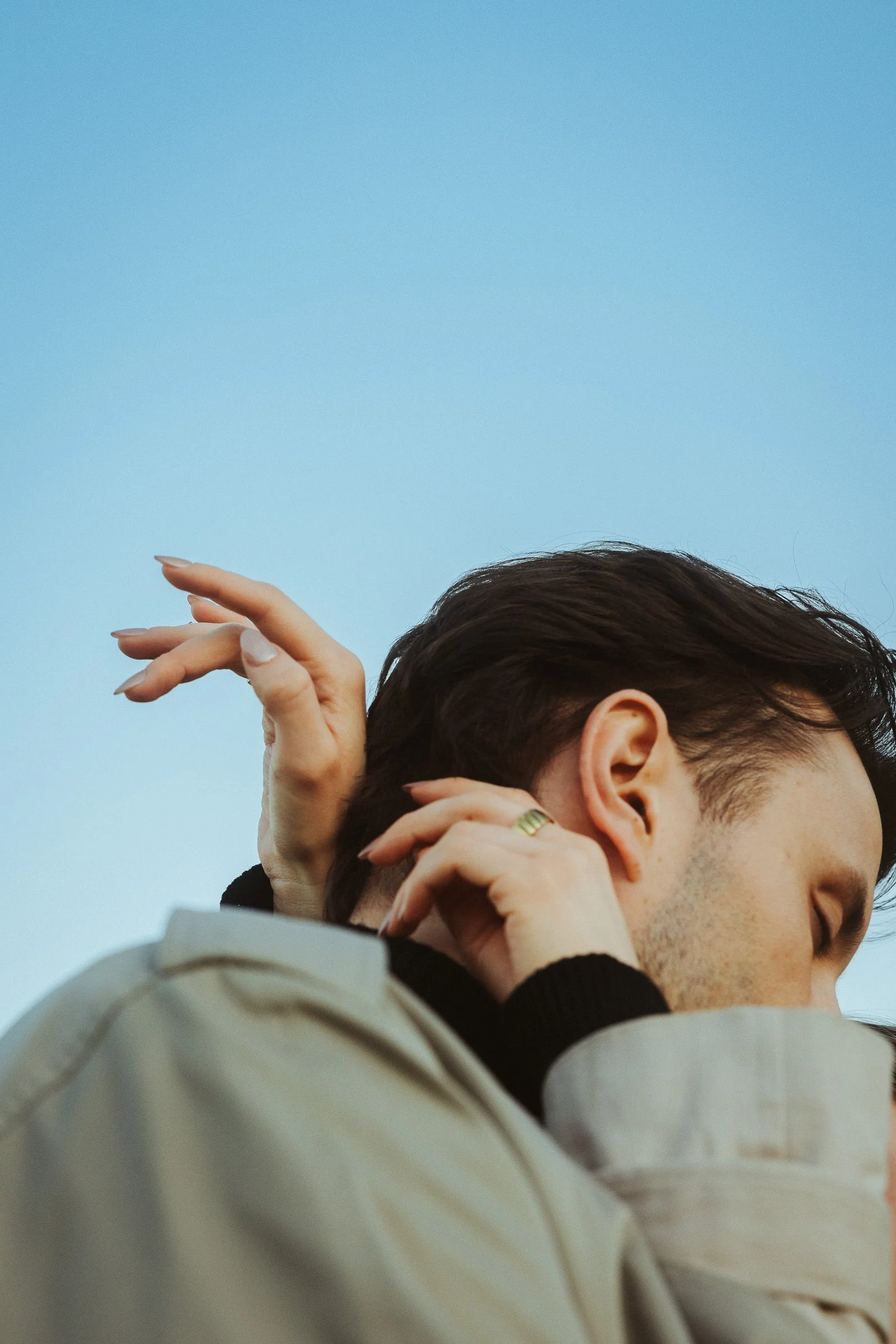 Nahaufnahme einer Person, die ihre Hand im Haar hat, mit einem blauen Himmel im Hintergrund.
