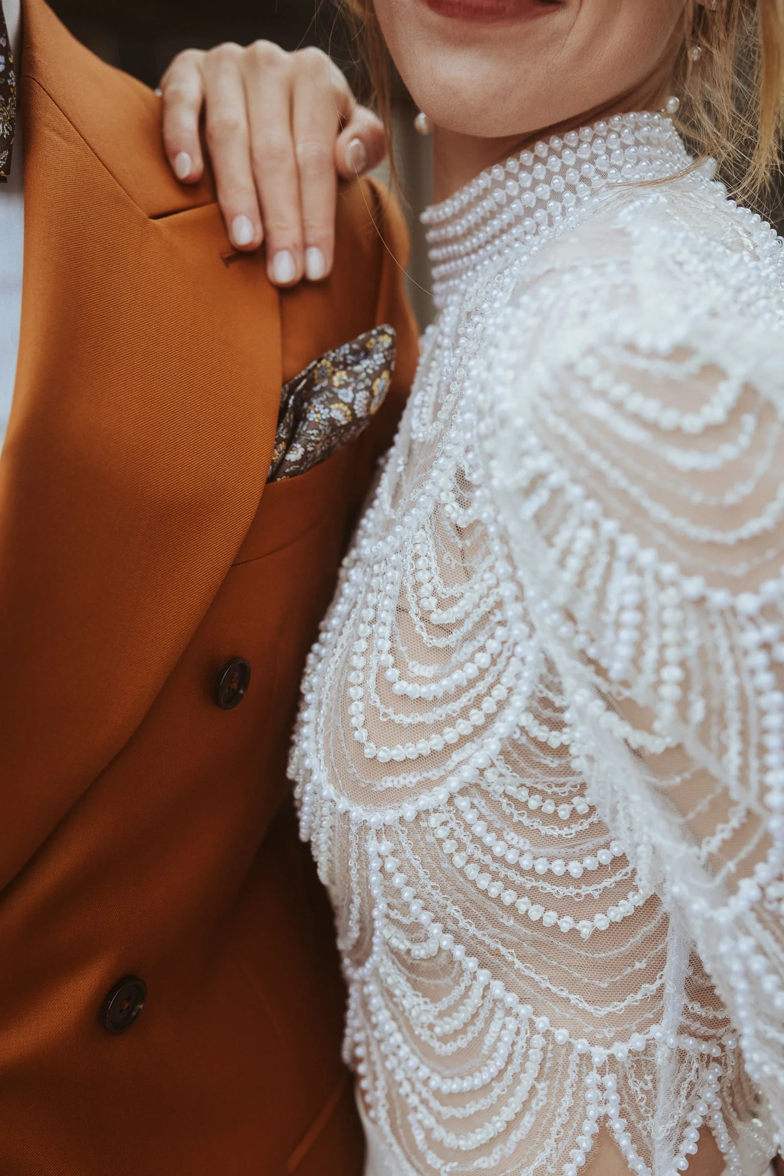 Detailaufnahme von perlenbesetztem Brautkleid und rostfarbenem Hochzeitsanzug bei einer urbanen Hochzeit in der Hafenkäserei in Münster