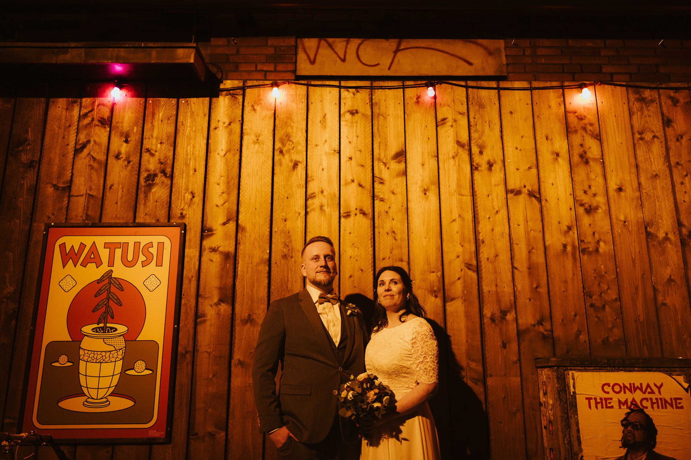 Hochzeitspaar in festlicher Kleidung vor einer Holzwand bei einer urbanen Hochzeit in Münster