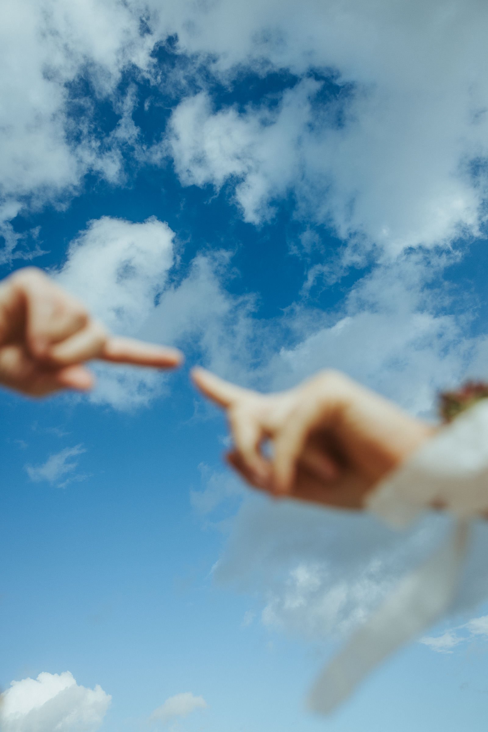 Zwei Hände, die sich in den Himmel strecken, vor blauem Himmel mit Wolken.